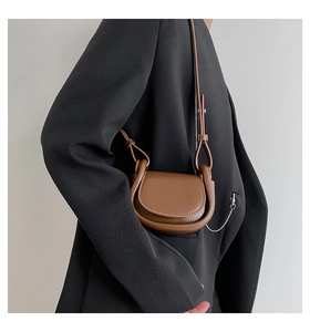 Detail view of a brown leather saddle bag on a black blazer with fine stitching and chain