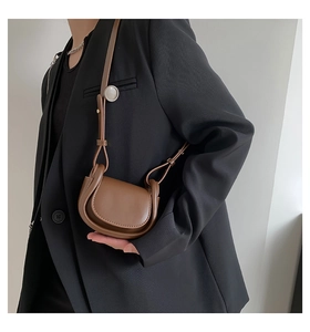 Close-up of brown leather mini saddle bag worn over black suit showing shoulder strap detail