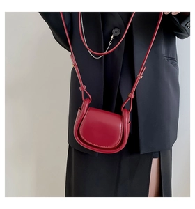 Close-up of a red leather mini saddle bag with golden buckles on a black blazer outfit