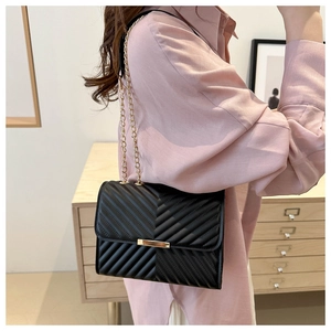 Detail of black quilted shoulder bag with V-shaped texture and gold metal chain strap
