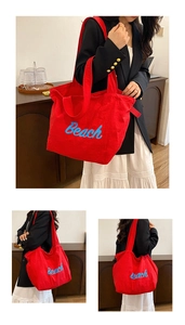 Detail of red canvas tote bag featuring navy blue Beach embroidery and soft texture