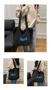 Detail of black nylon tote bag featuring blue Beach text embroidery and wide shoulder strap