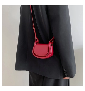 Detail of red leather mini saddle bag worn as crossbody over a black suit blazer
