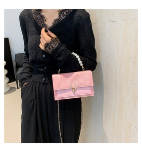 Détail du sac bandoulière tissé rose avec poignée en perles et chaîne dorée sur un modèle