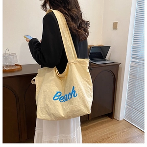 Close-up of a large pale yellow tote bag with blue Beach print worn over the shoulder