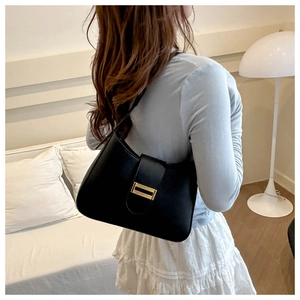 Minimalist black leather underarm bag with gold buckle shown on a model's shoulder