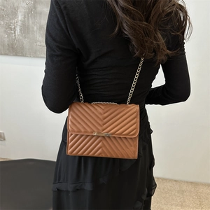 Minimalist V-quilted brown crossbody chain bag styled with an elegant black dress