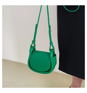 Detail of green leather saddle bag on black dress, showing shoulder strap and sleek texture