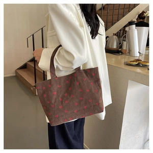 Sac cabas en velours côtelé marron avec broderie fraise porté par un mannequin
