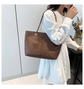 Detail of vintage brown patchwork tote bag with gold chain strap on model's shoulder
