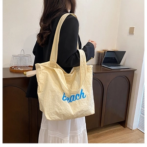 Detailed close-up of a large beige canvas tote bag with blue Beach letter printing