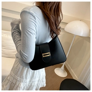 Detail of a black leather underarm bag with a gold metal buckle worn by a model