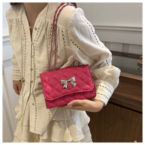 Detail of rose pink quilted crossbody bag featuring a silver metal bow and chain strap