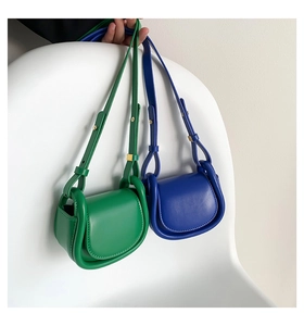 Detail of mini leather shoulder bags in green and blue hanging on a minimalist white chair