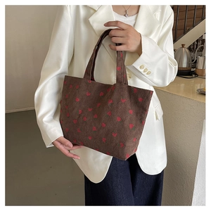 Détail du motif fraise sur un cabas en velours côtelé marron porté par un mannequin