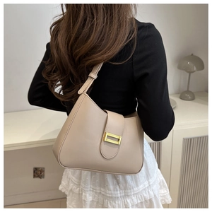 Minimalist beige leather hobo bag with gold buckle shown on shoulder for daily commute