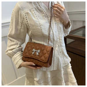 Close-up of brown quilted chain bag featuring a silver bow buckle and detailed stitching