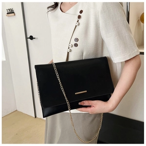 Detail of minimalist black envelope clutch featuring a gold metal bar and delicate chain strap