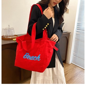 Detail of red canvas tote bag with blue Beach lettering and thick shoulder straps