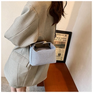 Side view of light blue denim crossbody bag with metal clasp worn with a grey blazer