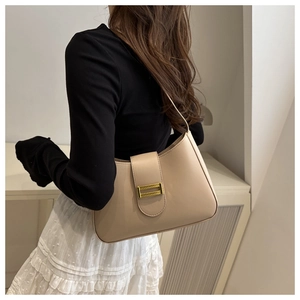 Detail of cream baguette shoulder bag with gold clasp shown on a shoulder