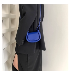 Detail of a bright blue mini leather saddle crossbody bag worn on a black suit blazer