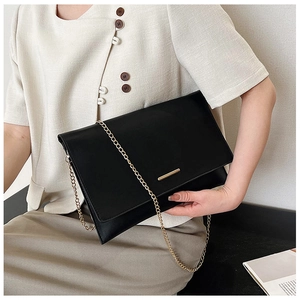 Side view of black envelope clutch with gold chain strap worn by a female model