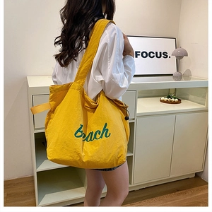 Close-up of bright yellow nylon tote bag featuring green Beach script on the side