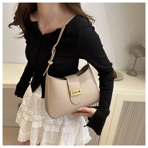 Detail of beige faux leather baguette bag featuring a gold buckle on a model shoulder