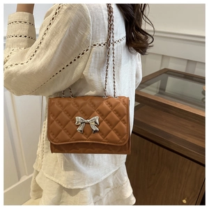 Brown quilted leather chain bag with silver bow accent worn by a woman from a side view