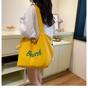Side view of model wearing a large yellow nylon tote bag with green Beach print