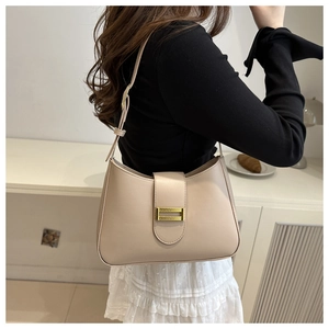 Detail shot of a beige crescent underarm bag featuring a golden metallic buckle on a model