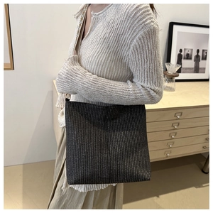 Détail d'un sac cabas tissé gris foncé avec large bandoulière dans un décor de style épuré