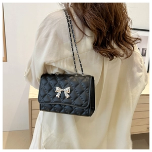 Detailed view of black quilted crossbody bag with silver bow accent on model's back