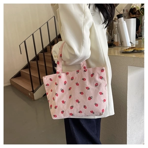 Sac fourre-tout en velours côtelé à imprimé fraise porté par un mannequin en café