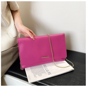 Detail of fuchsia rectangular clutch with gold metal bar and slender chain strap