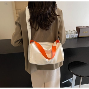 Detail of white minimalist crossbody bag with orange contrast handles and wide shoulder strap