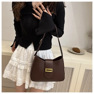 Detail of dark brown baguette bag with gold buckle worn on shoulder in a lifestyle setting
