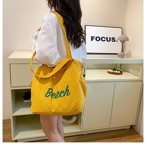 Detailed view of yellow nylon tote bag with green Beach print on a shoulder-carried model