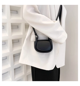 Close-up of minimalist black leather mini saddle bag with thin shoulder strap on model