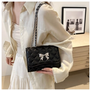 Detail of black quilted crossbody bag featuring a silver bow buckle and chain strap