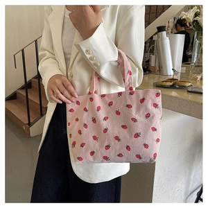 Détail du sac cabas en velours côtelé rose à motif fraises dans un café chaleureux