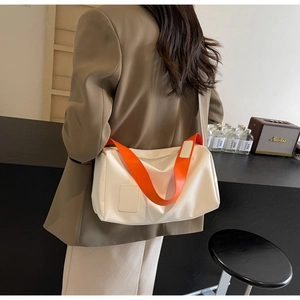 White crossbody bag detail with bright orange wide strap and glossy leather finish