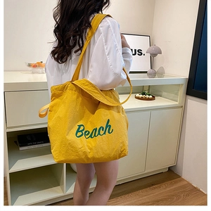Detail of yellow canvas tote bag featuring green Beach lettering and dual strap handles