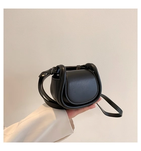 Detail of a vintage black leather mini crossbody saddle bag held by hand in a studio