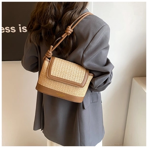 Detail of hand-woven straw shoulder bag with brown leather strap and knotted accents