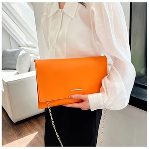 Close-up of bright orange envelope clutch with gold metal bar and delicate chain strap