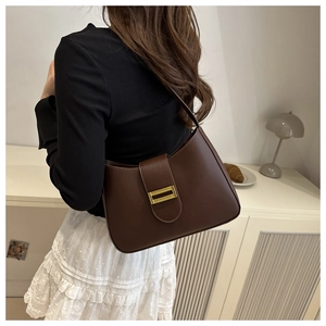 Close-up of a dark brown faux leather underarm bag with a golden metal buckle on a shoulder