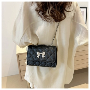 Detail shot of black quilted crossbody bag with silver bow hardware worn by a model