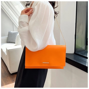 Detail of bright orange rectangular crossbody bag with gold bar buckle and chain strap